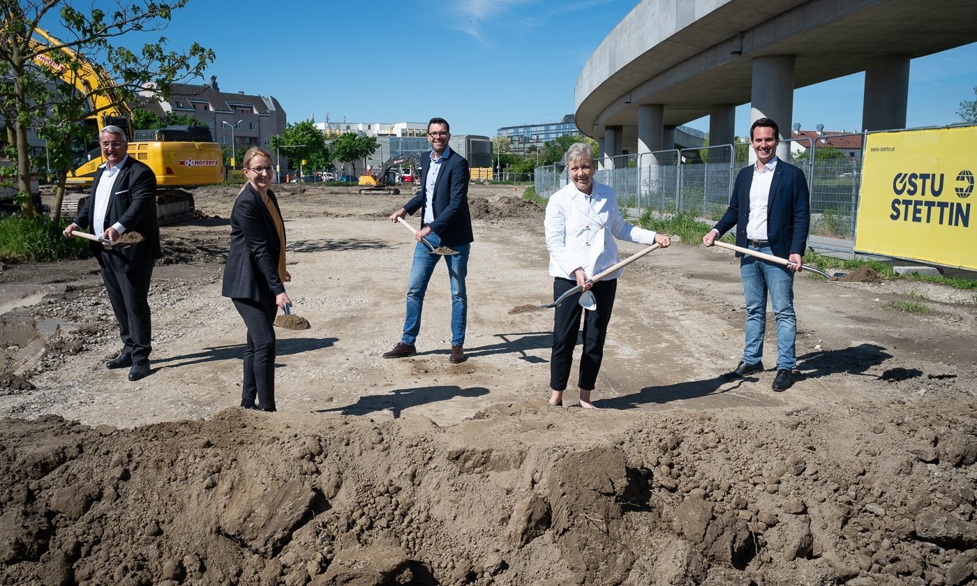 5 Personen stehen um eine Baugrube mit Spaten in der Hand 