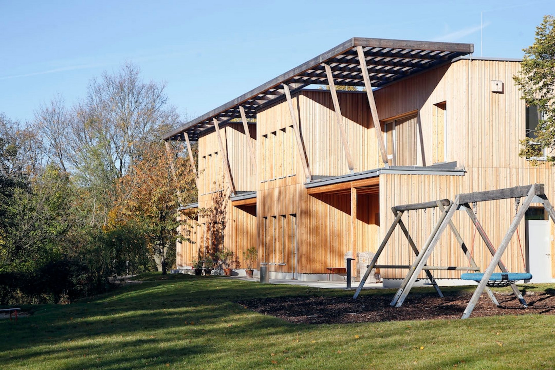 Moderner Holzbau im Grünen mit einer Schaukel davor