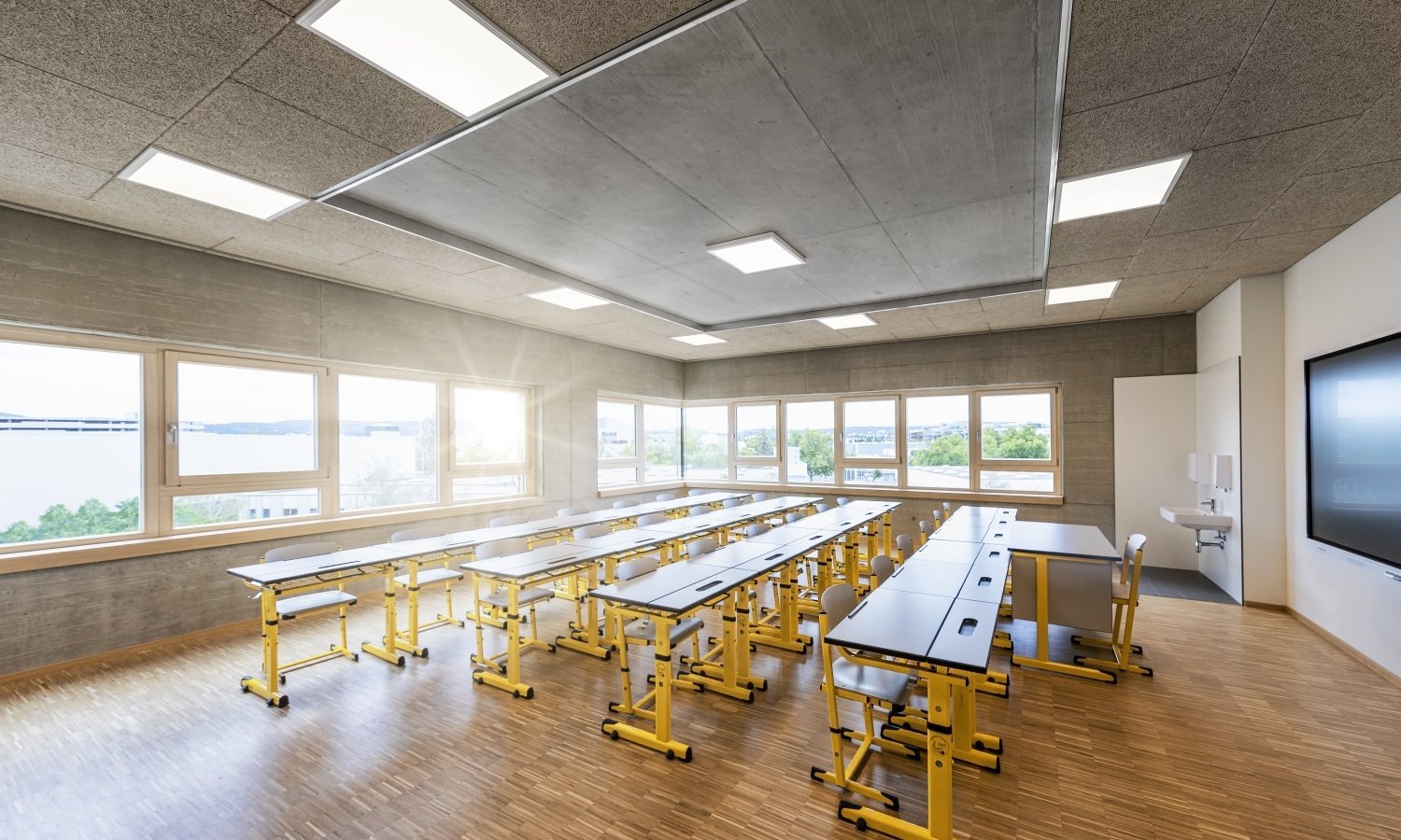 Modernes helles Klassenzimmer mit Schultischen und gelben Sesseln