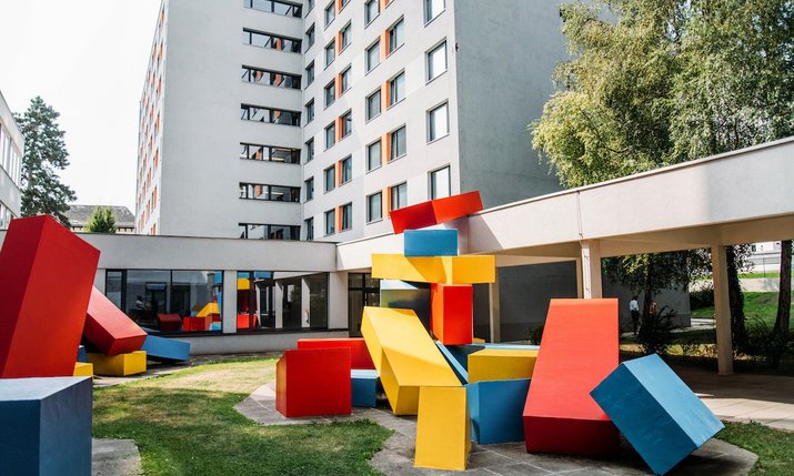 7-stöckiges weißes Gebäude mit buntem Kunstwerk im Vordergrund
